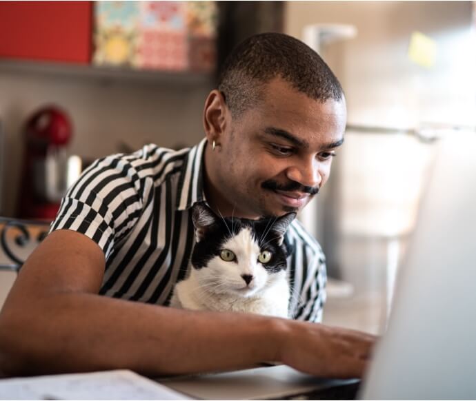 猫を抱えながらノートパソコンを使用している男性