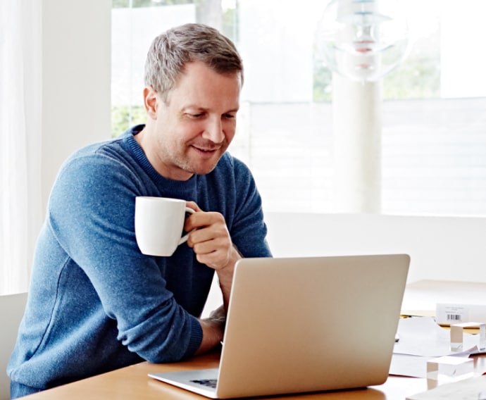 自宅でコーヒーを飲みながらノートパソコンを使用している男性。